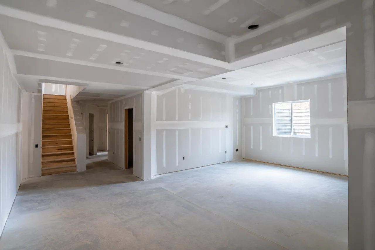 Finished basement drywall — taped and mudded walls and ceiling with a bare concrete floor and open stairway